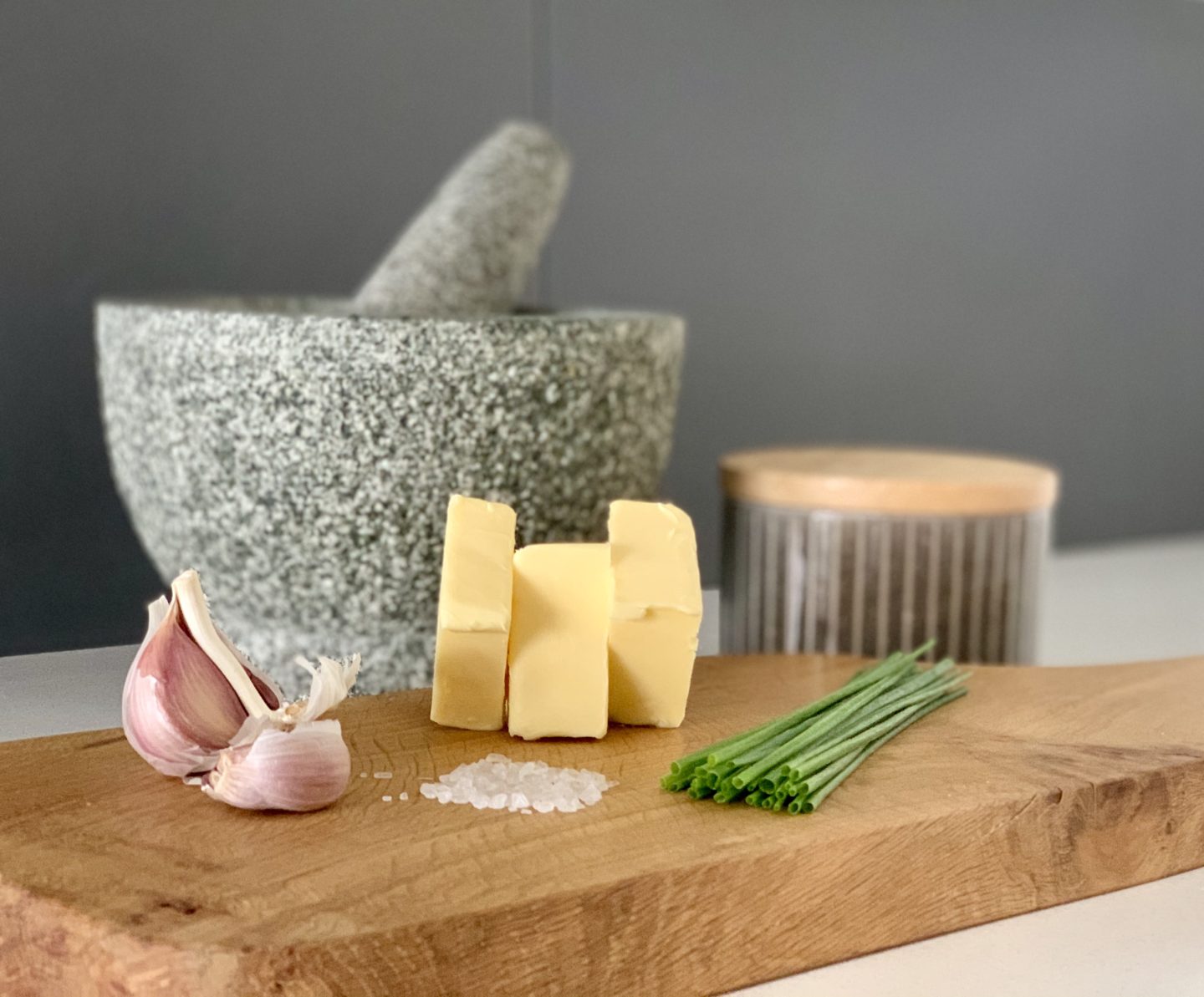 Garlic, chive and herb butter cut into slices on a chopping board with sea salt and pestle and mortar