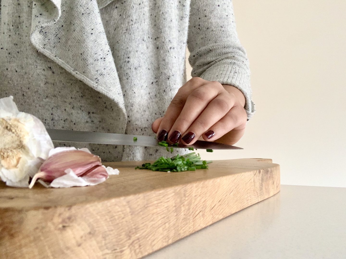 Bejal chopping chives on a chopping board with cloves of garlic atthe side.
