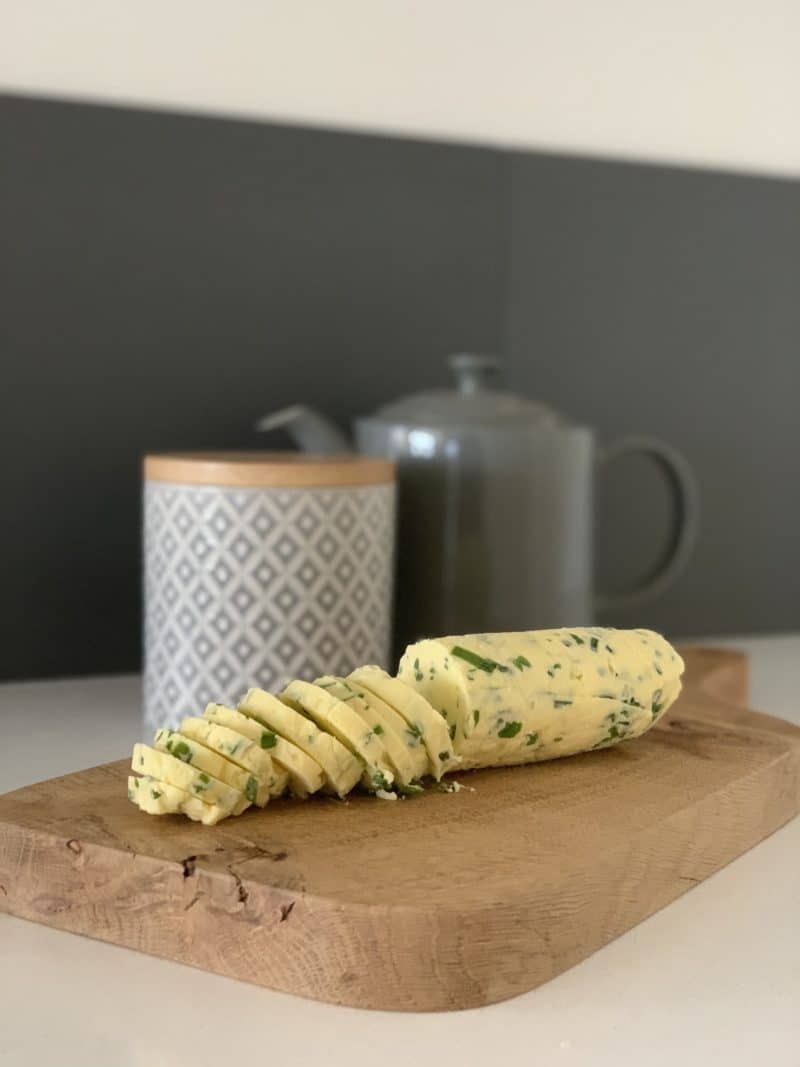 Garlic, chive and herb butter cut into slices on a chopping board