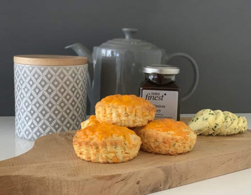 Red Leicester topped cheese scones with garlic and herb butter and onion chutney on a chopping board.