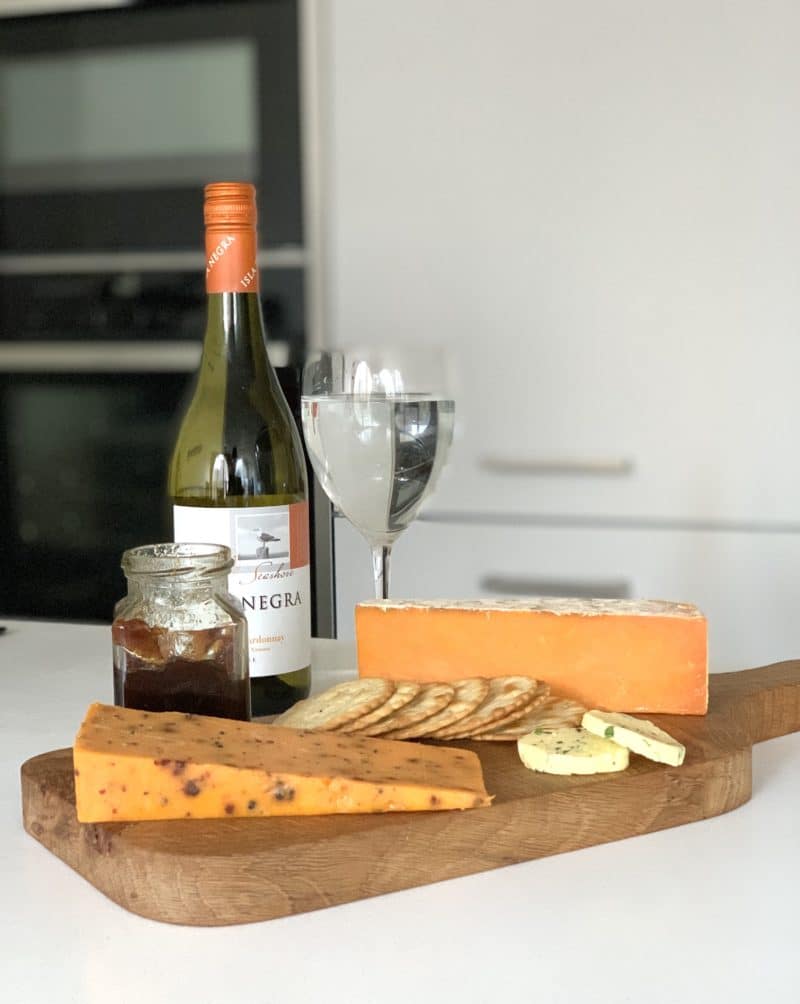 Chopping board with Sparkenhoe Red Leicester, biscuits, red onion chutney jar, Red Leicester with chilli and a bottle of white wine