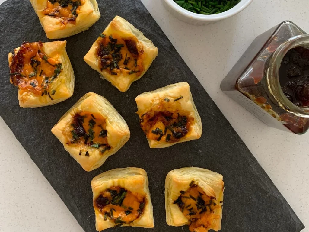 Red onion and Red Leicester cheese tarts on a slate board with red onion chutney jar on the site