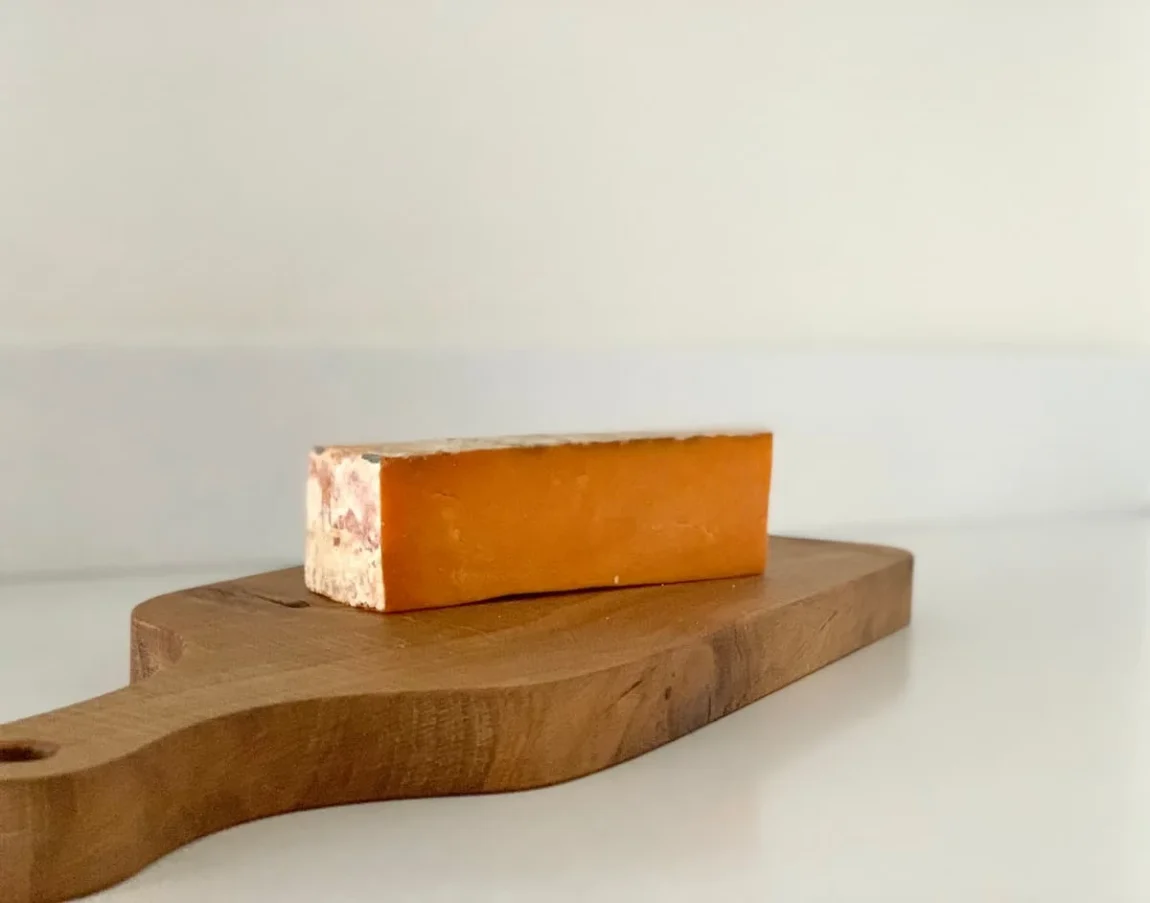 Sparkenhoe Red Leicester cheese slice on a chopping board with a white background