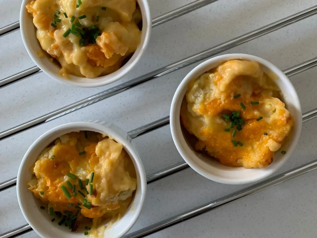 Top lay of 3 Red Leicester cheese cauliflower cheese in white ramekins on a silver rack.