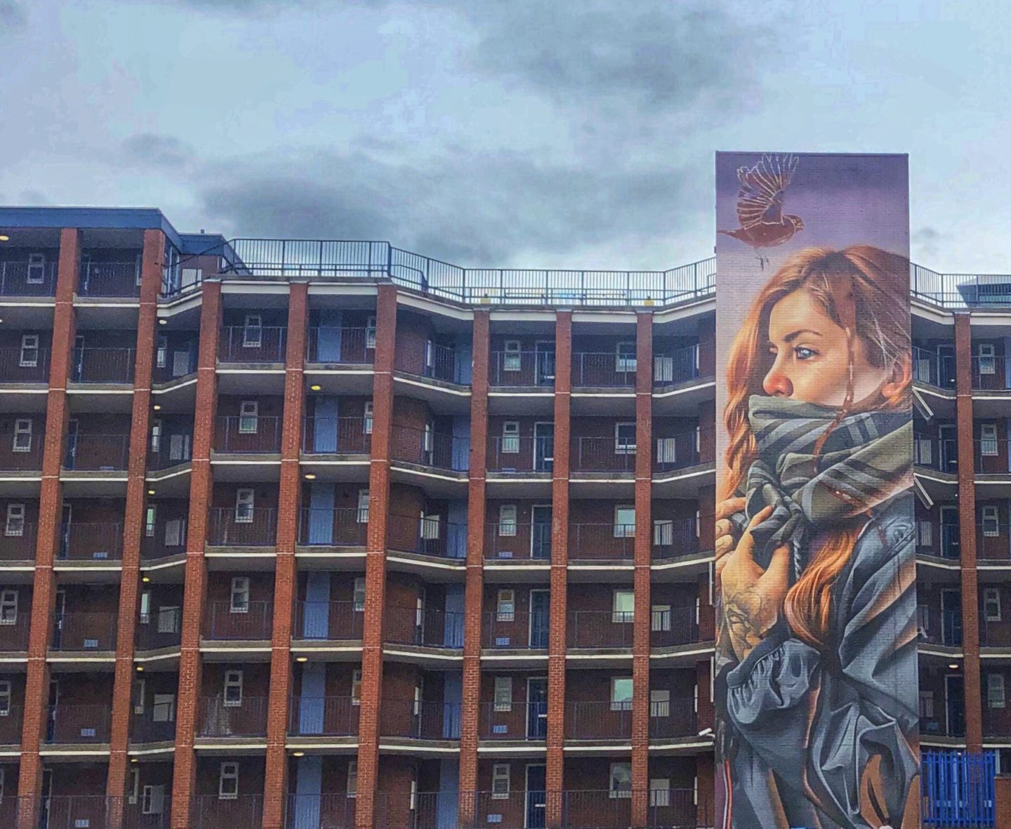 Street art of a girl with a blue and checked scarf around her neck on the frontage of red brick apartment buildings on Yeoman Street, Leicester
