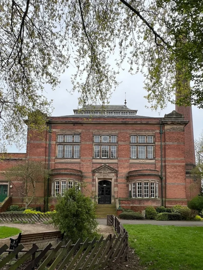 Exterior of Abbey Pumping Station Museum  surrounded by shrubs and trees. The building is made from brown brick with silver rimmed windows