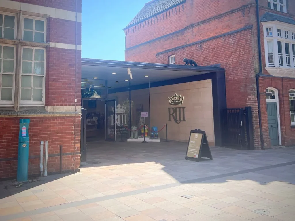 Exterior of King Richard III Visitor Centre with a glass frontage and gold KRIII sign on the white tiled wall