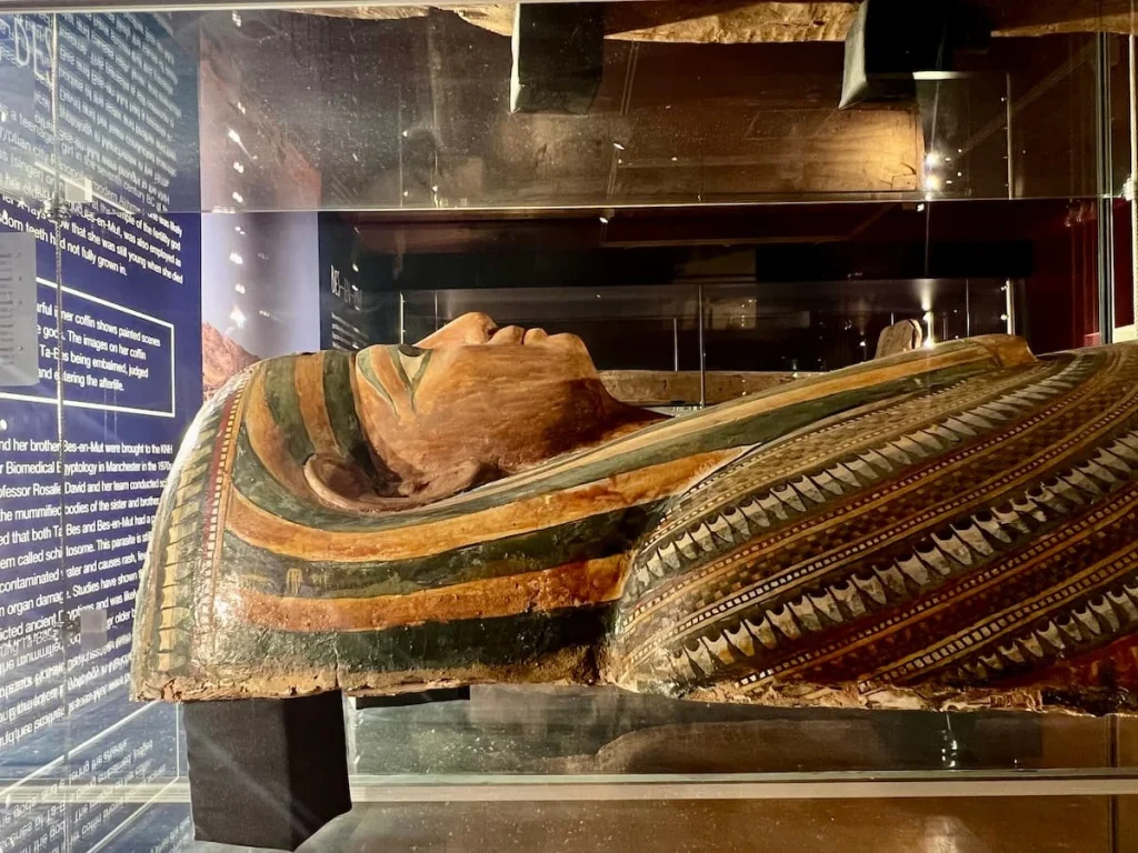 Mummy tomb in a glass cabinet in traditional colours of black, browns and greens and gold at New Walk Museum and Art Gallery, Leicester