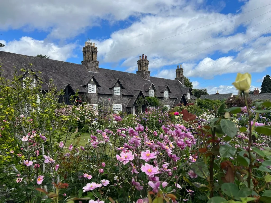 A row of cottages in Woodhouse Eaves that are set back from the road with gardens that are covered in pretty floral s that are green, pink and yellow. Image taken in summer