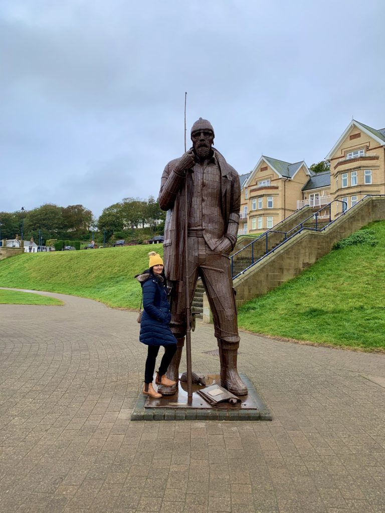 Bejal standing next to the statue of a sailor in Filey
