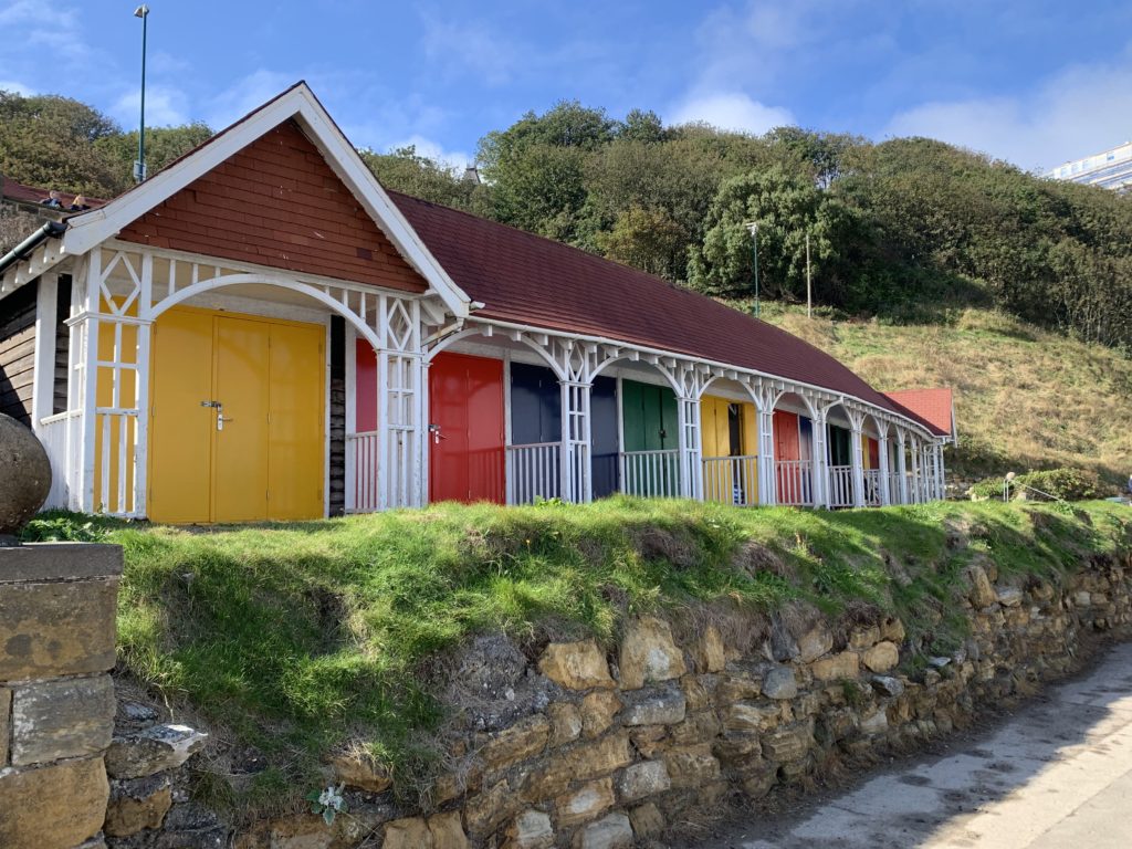 North Yorkshire Coastal Road trip: Scarborough colourful beach huts on an elevation on the beach. Colours range from red, yellow and green