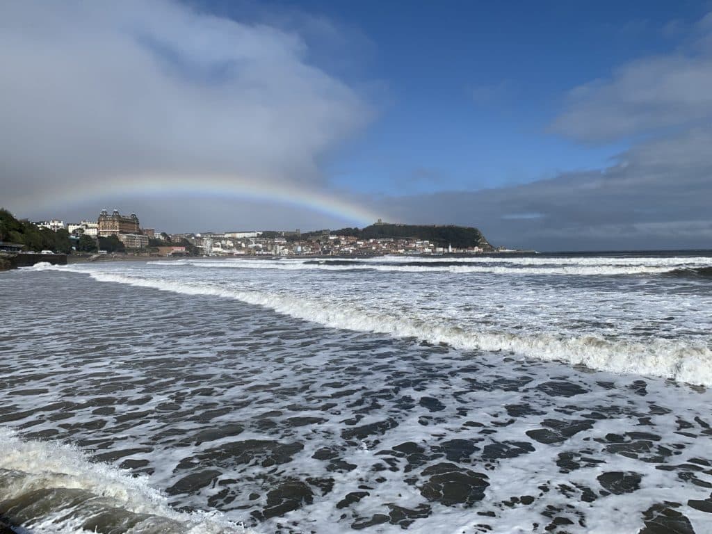 Scarborough sea front with waves crashing on the beach and a rainbow in the distance