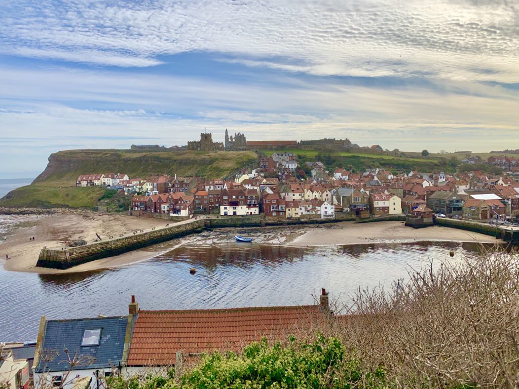 Whitby coastal area with a pier and the town with Whitby Abbey on th ehill