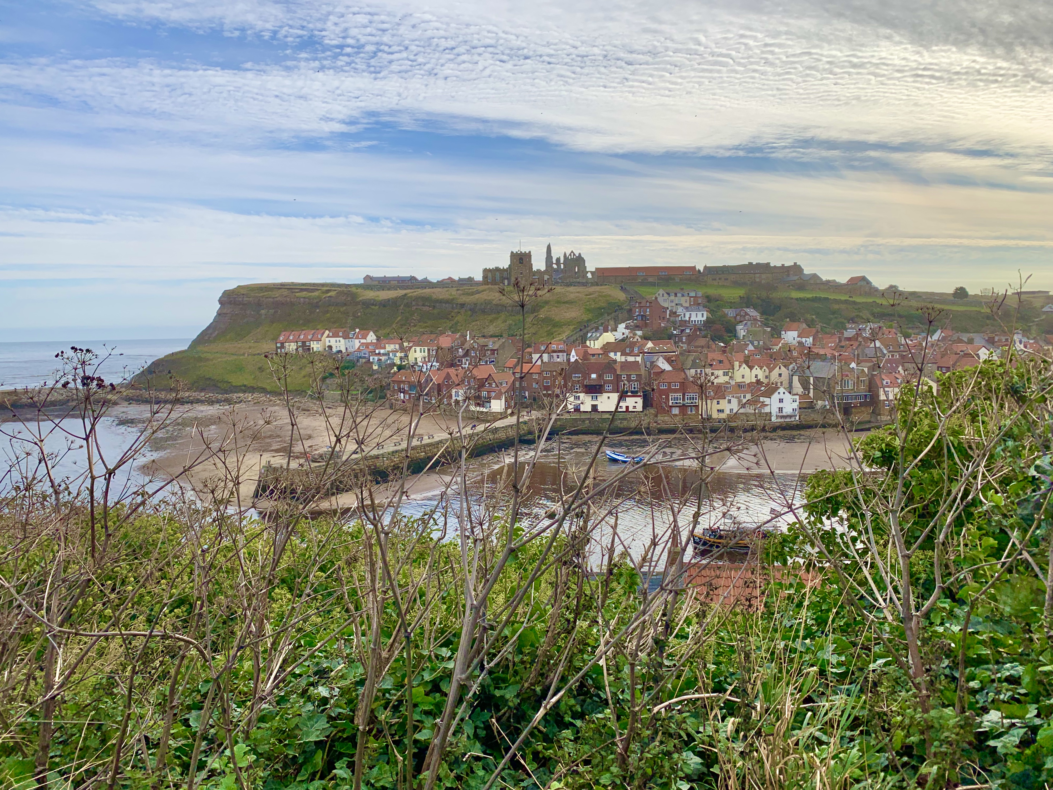 North Yorkshire coast road trip, Whitby houses with Whitby Abbey in the background surrounded by the sea and a blue cloudy sky