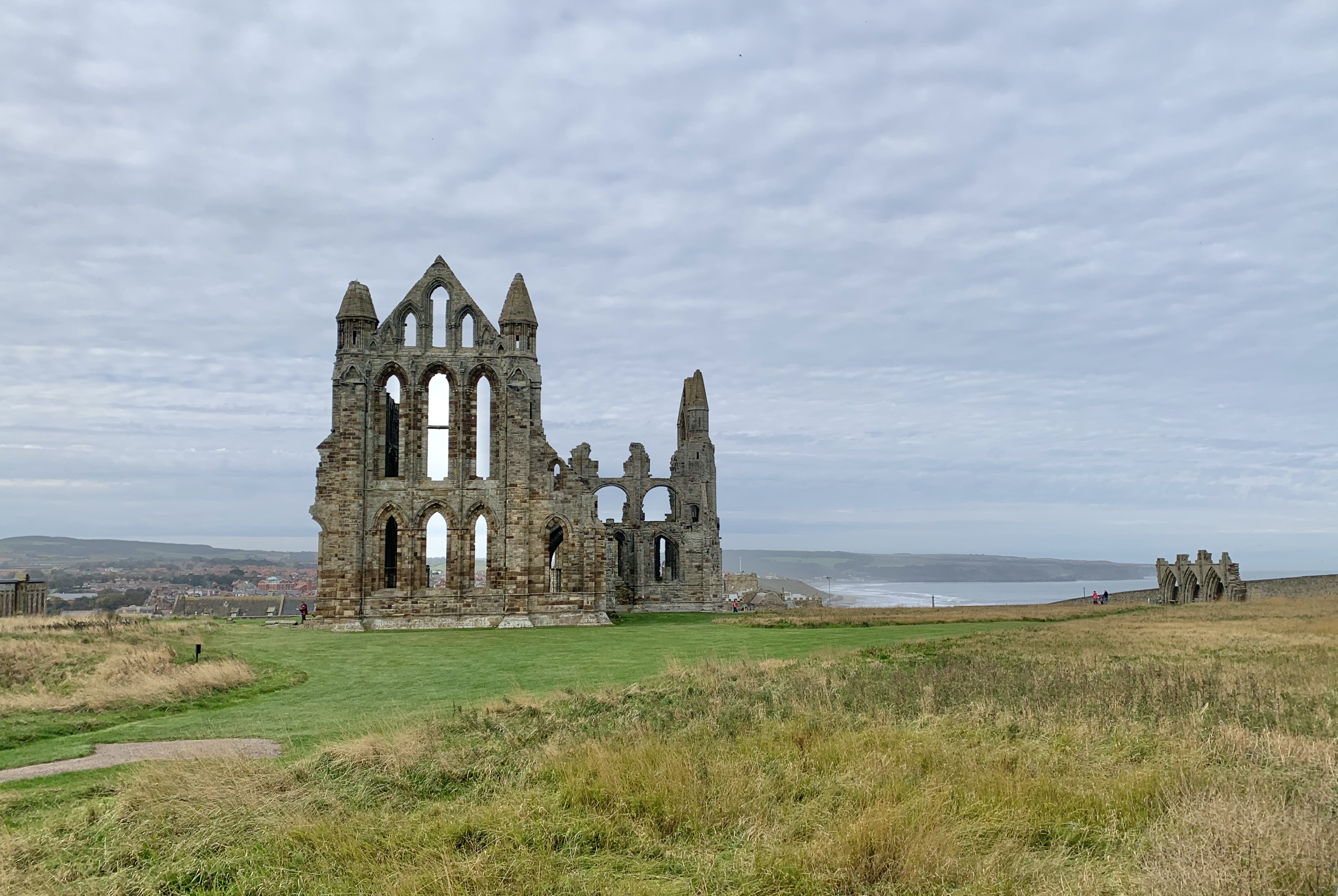 Whitby Abbey ruins made from grey stone, from a distance with grass all around and the sea in the background
