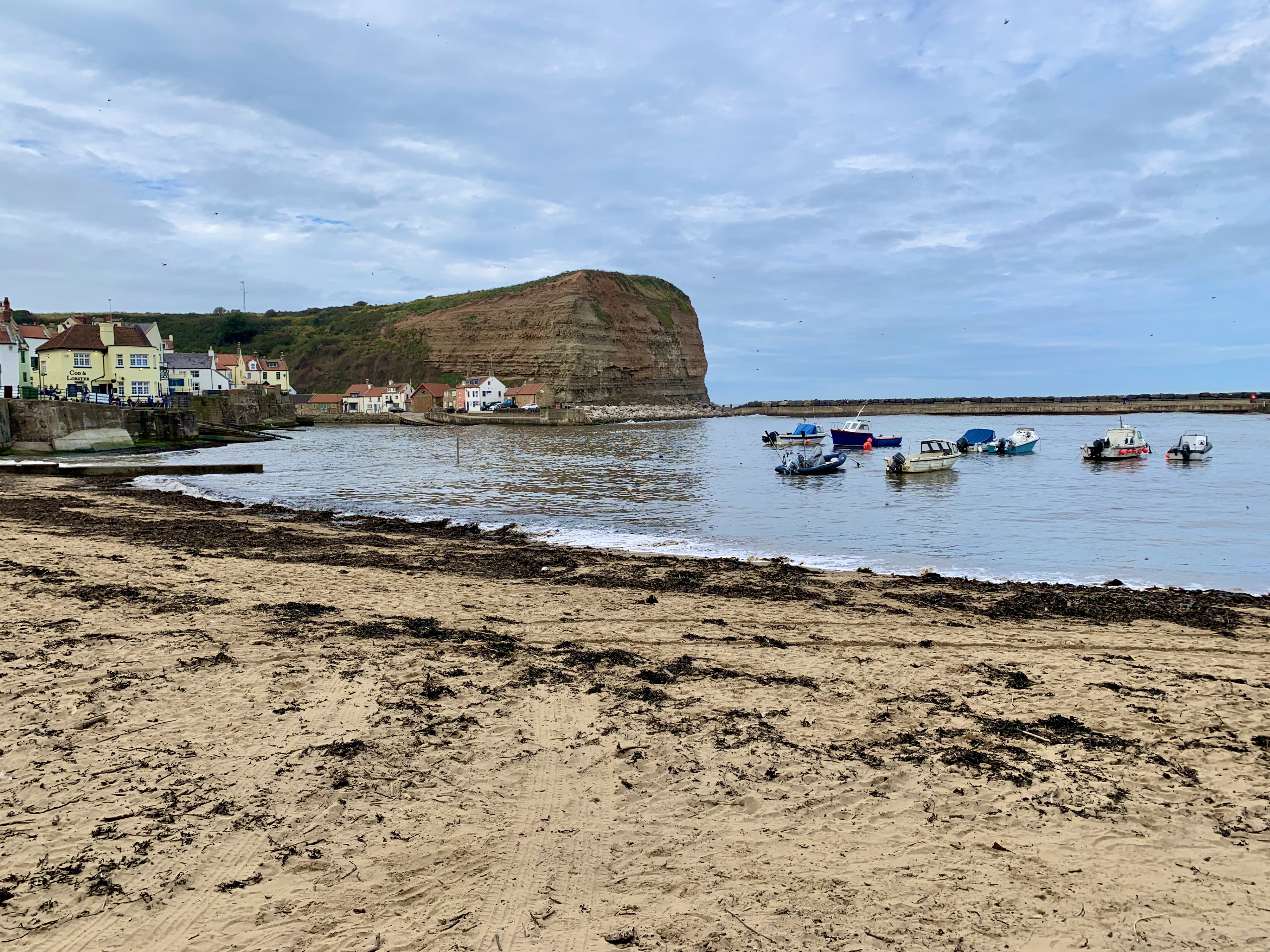 Staithes waterfront with fishing boats in the distance and a brown cliffs