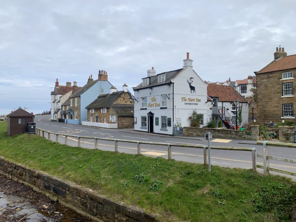 Sandsend Hart Inn pub with houses to the side and a wooden bus stand 