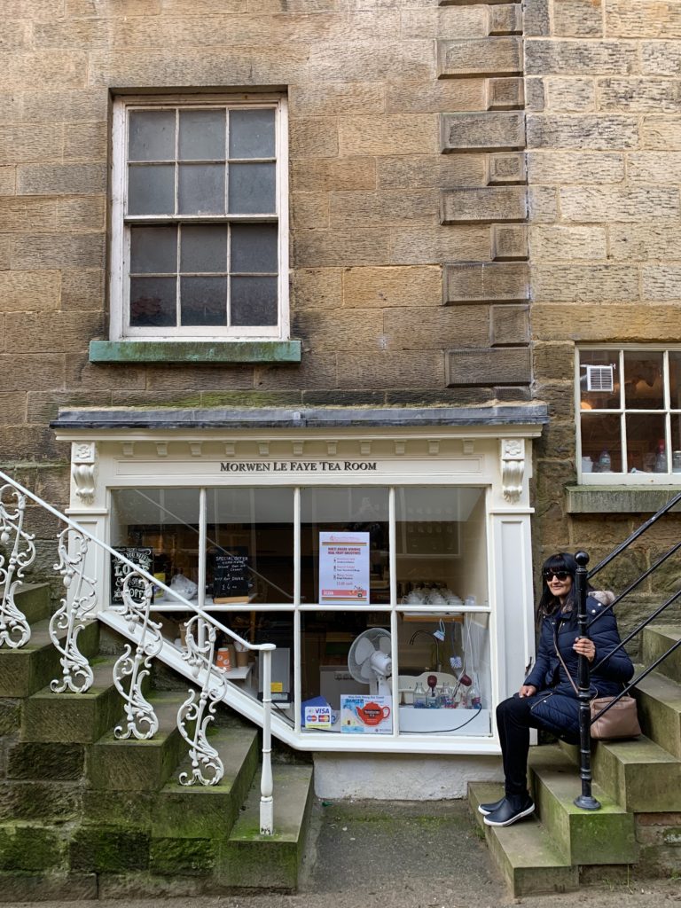 Robin Hood's Bay Tea rooms with Bejal sitting on the steps outside wearing a blue winter coat