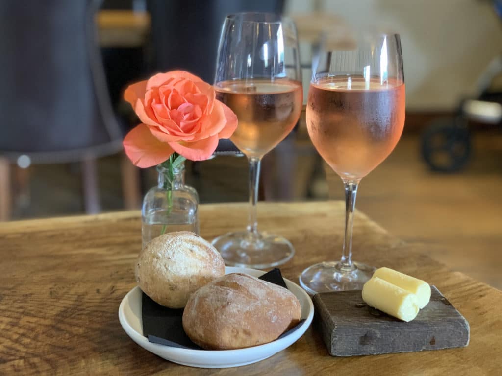 The Wildebeest, Norfolk Bread rollsin plate with 2 small rolls of butter and 2 cold glasses of rose wine ona wooden table.