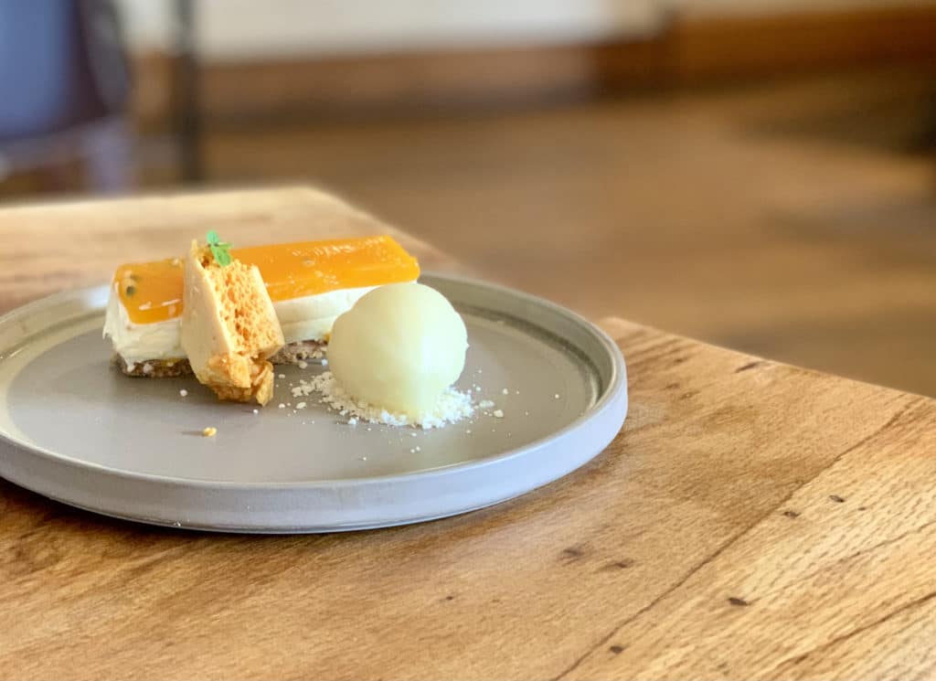 The Wildbeest dessert of passionfruit cheesecake with honeycomb sorbet on a grey plate on a brown wooden tabel in Norfolk.