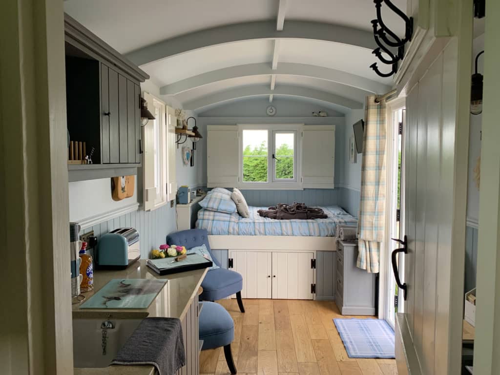 Willowfen Retreat Interiors with teh checked blue and white bed linen and dining area plus seats and TV on the wall, Norfolk
