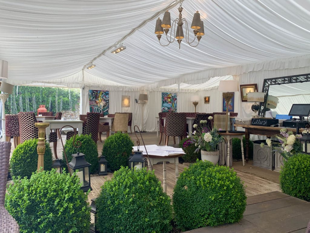 vegetarian-friendly places to dine in Norfolk: The Wiveton Bell Interiors with topiary plants, tabels and chairs and a wooden floor in a white marquee set-up.