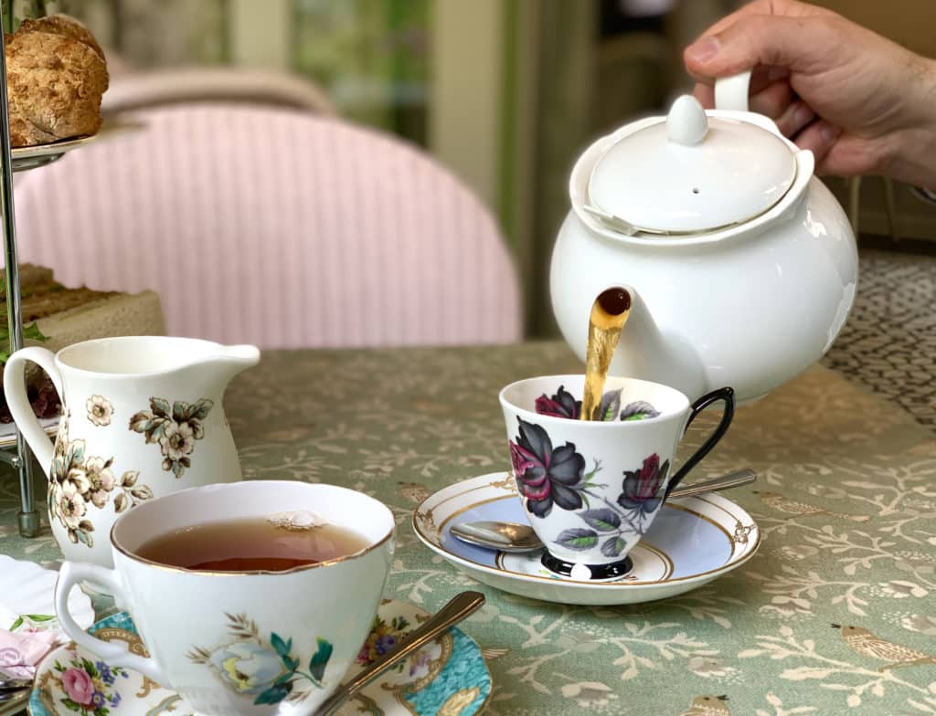 The Folly Tearooms, Norfolk tea being poured into a floral china tea cup with a pink upholstered chair in the background
