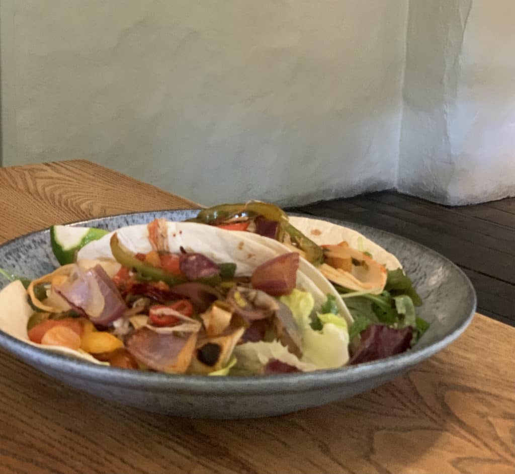 Banana blossom, soft tacos, baby gem, tomato, red onion and spicy sriracha  at Kings Head in Bawburgh, Norfolk. The plate is grey and black speckled on a light wooden table