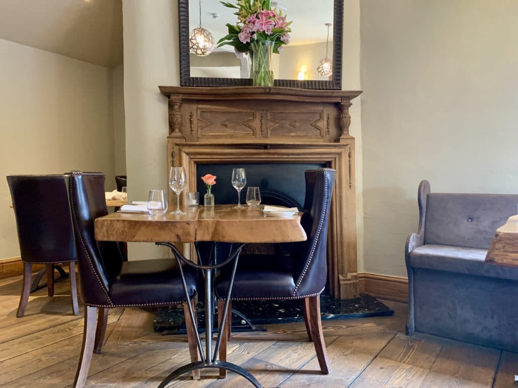 Vegetarian-friendly places to dine in Norfolk: The Wildebeest Interiors with a brown wood old fireplace in the background and a bog wooden table with dark blue upholstered leather chairs with long backs