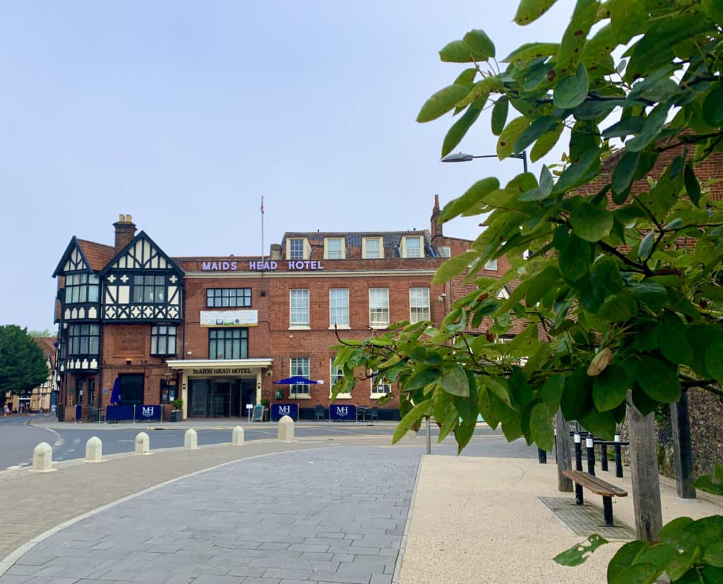 The exterior of teh historic Maid's Head Hotel , Norwich. Leaves are partially covering the right hand side of the hotel and there are Tudor style black and white elements to the architecture.