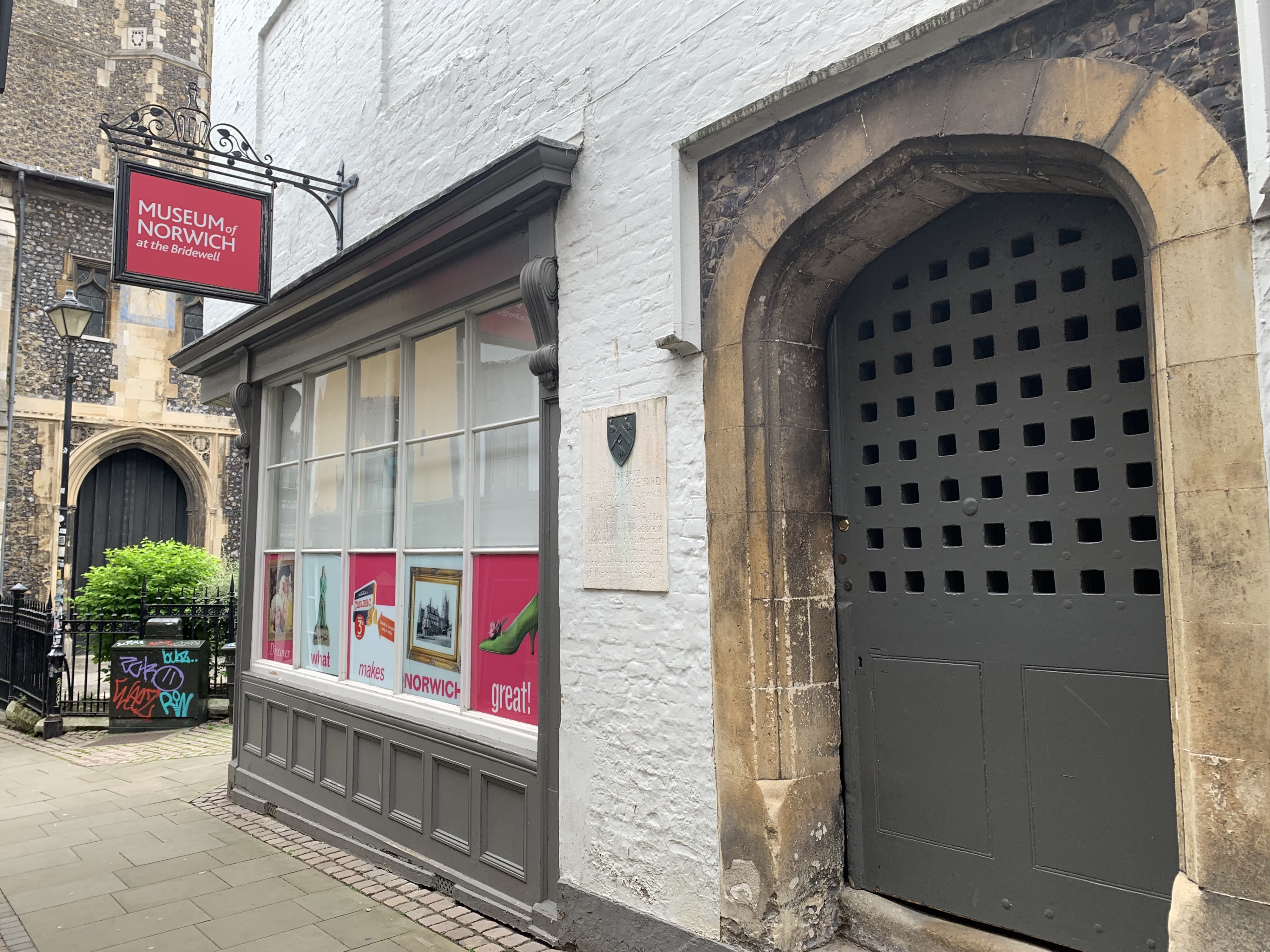 The exterior of the Museum of Norwich at The Bridlewell. There is a red sign with a medieval style brown door.