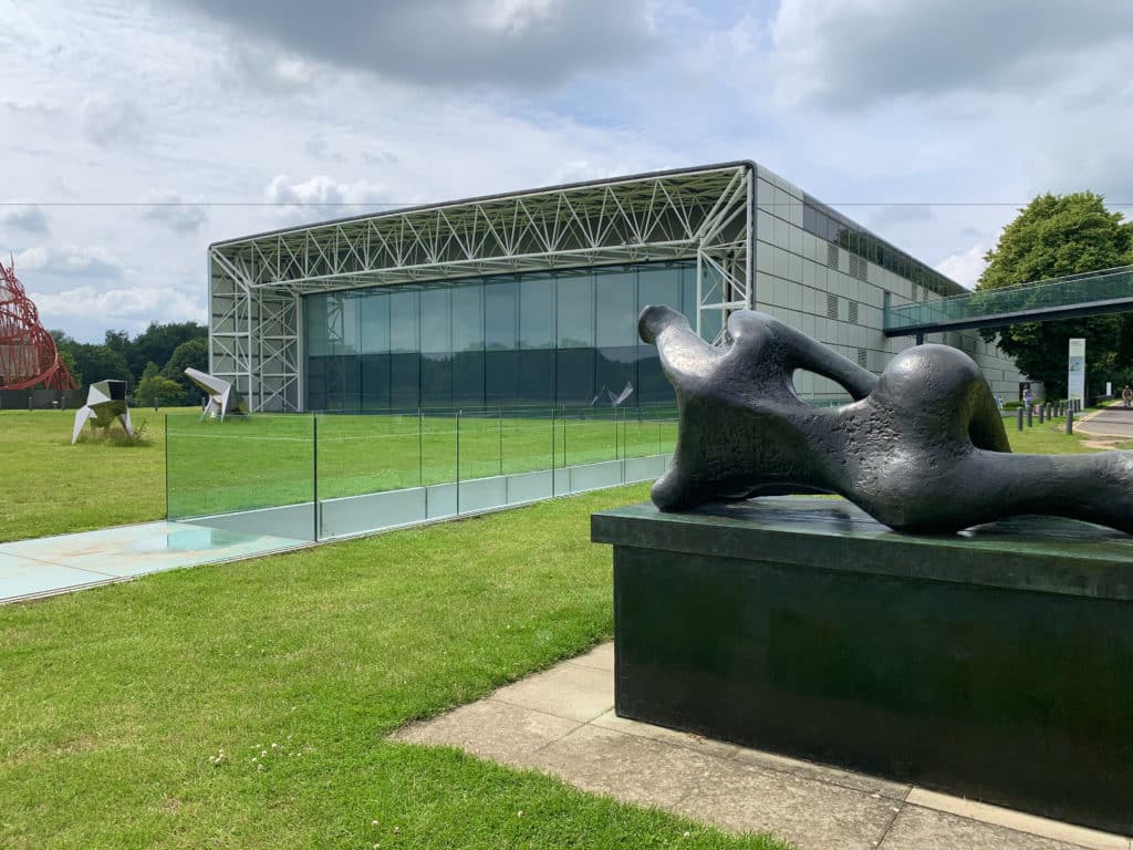 The exterior of the Sainsbury's Centre for Visual Arts. There is a lawna nd a modern building with sculptors on the lawn in Norwich.