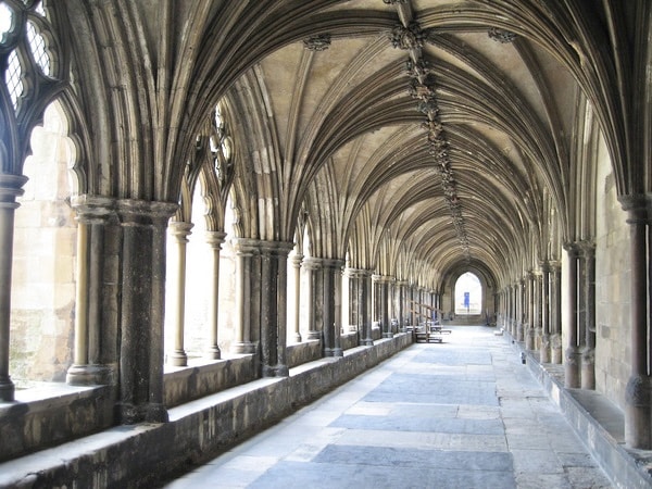 The cloisters of Norwich Cathedral with autumn light shining through and a paved floor