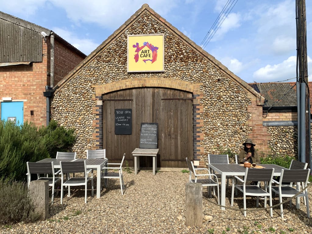The Art Cafe, Cley. Bejal is sitting enjoying a cup of coffee outside the cafe which has a pebble cladded exterior in Norfolk