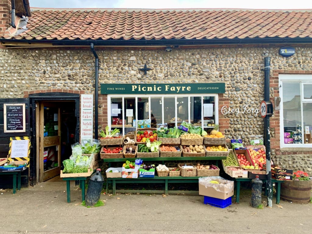 The pebble cladded exterior of Picnic Fayre in Cley, Norfolk. There are baskets of fruit and vegetables outside the deli in Norfolk