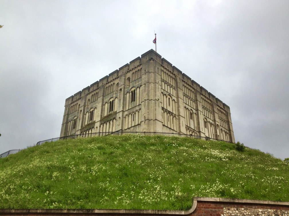 The exterior of Norwich Castle which sits on a grass mound. The sky behind is grey.