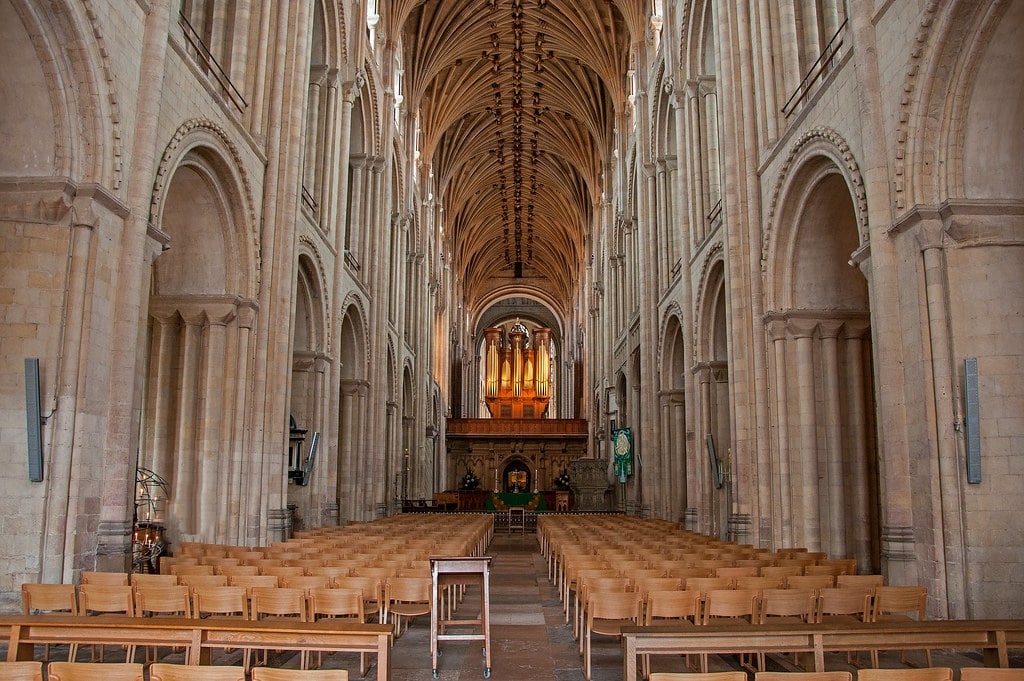 The interior of Norwich Cathedral with its gothic structure and main alter. There are seats at either side of the alter.