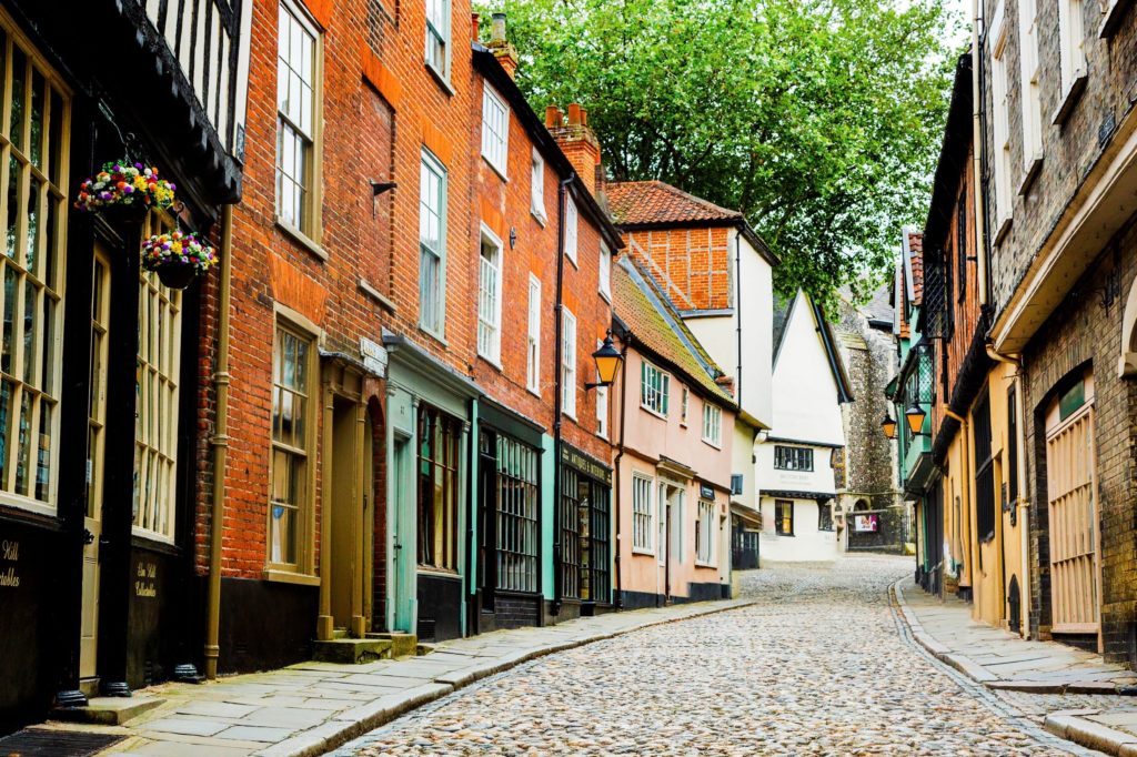 Elm Hill with colourful shops on either side and cobbled stone streets with a slight incline heading up towards the centre of Norwich shopping area.