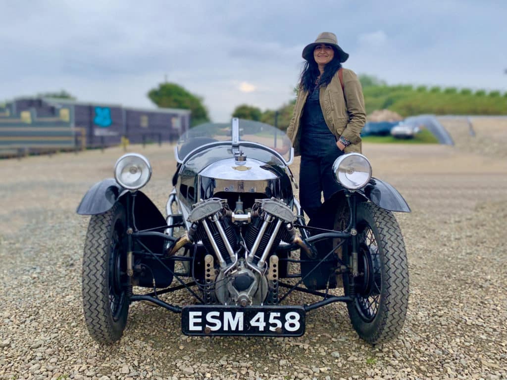 Bejal wearing a khaki jacket and matching hat standing in Morston Quay next to a Classic Cars