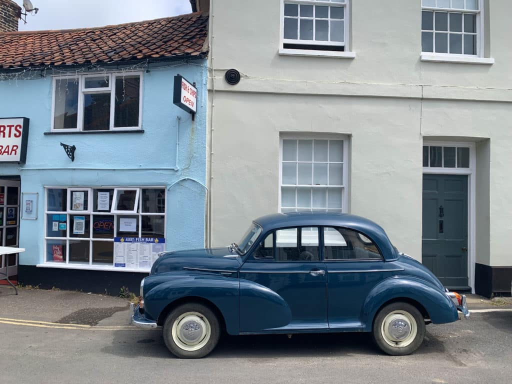Morris Minor car in tea; parked outside a Fish & Chip shop in Holt, Norfolk. The building in the background has a pale blue exterior and is teh Fish & Chip shop.