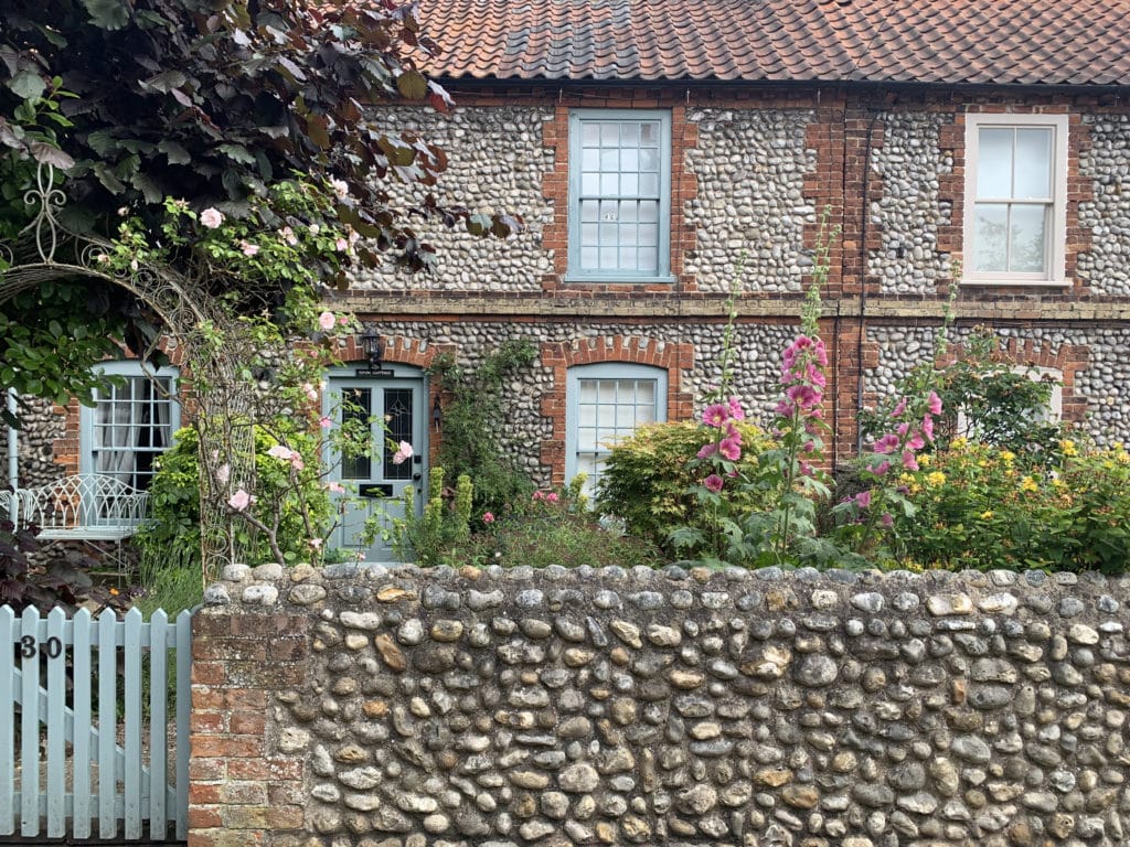 Holiday cottages in Holt with sage green painted windows and doors, lots of pretty foliage and flowers in the front garden and a pebble cladded exterior wall