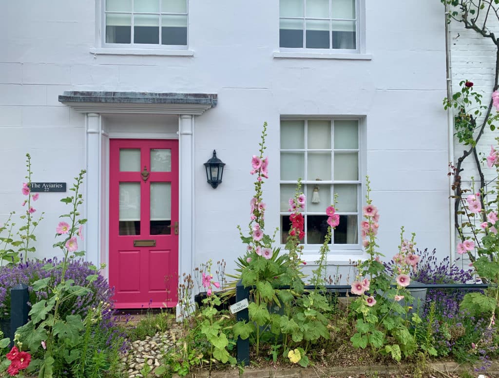 Pink front door with white painted bricks and pink, purple and green flowers in the front garden at a house in Burnham Market, Norfolk