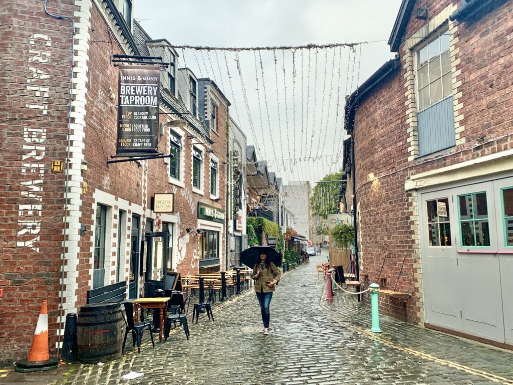 48 hours in Glasgow: Bejal walking down Ashton Lane with an umbrella. Shops and craft breweries along either side