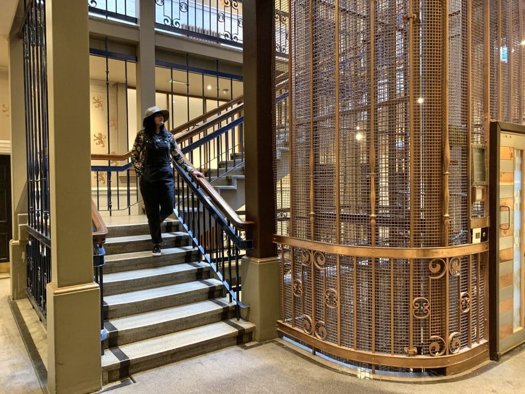 48 hours in Glasgow, ABode Hotel Glasgow Elevator wit Bejal walking down stairs wearing a hat and black dungarees. 