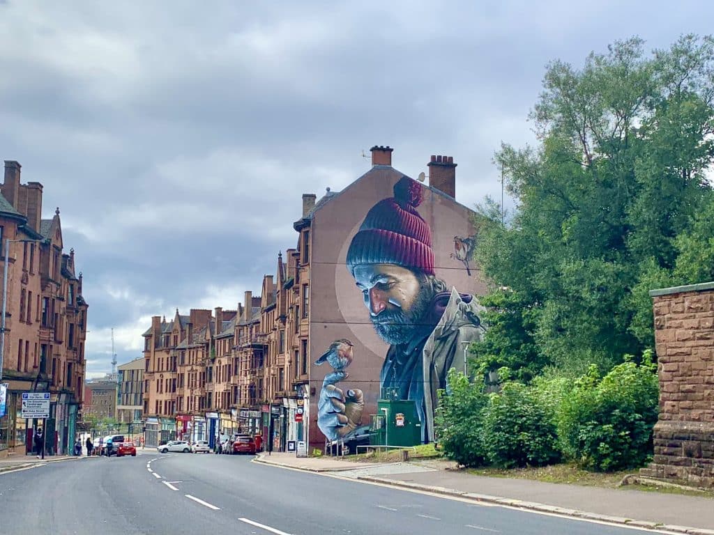 A mural of a man holding a bird perching on his hand in Glasgow. The mural is part if teh Glasgow Mural Trail