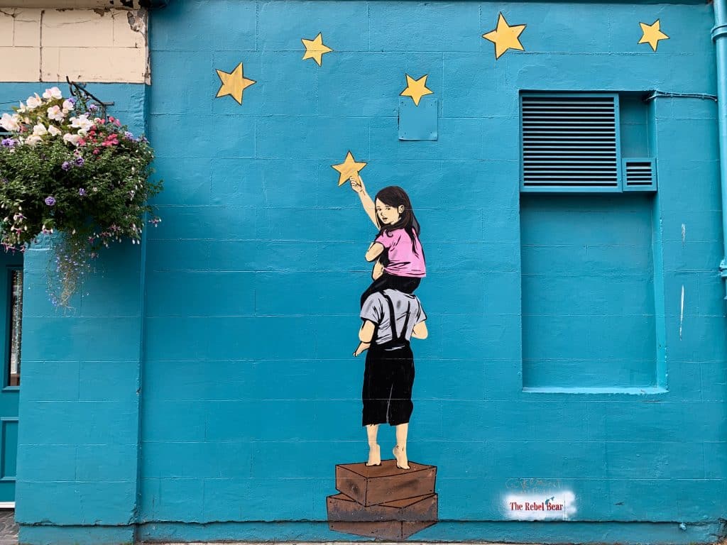 Glasgow Street Art of a girl sitting on a bows shoulders holding a gold star. The background is turquoise.