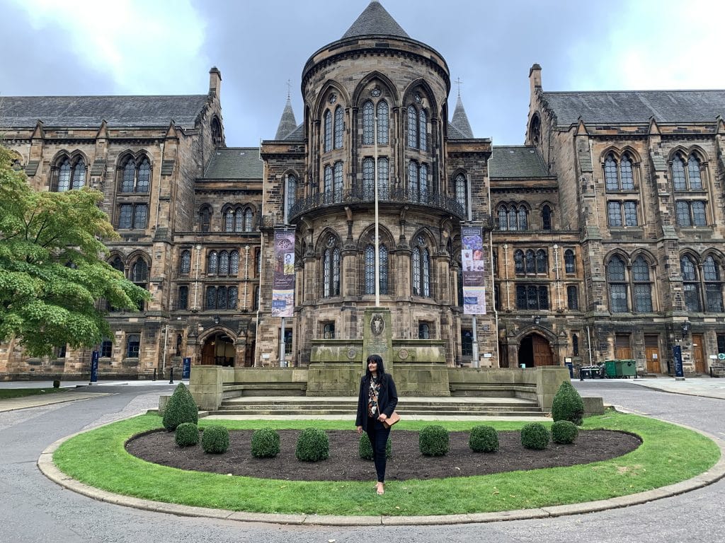 Bejal standing in the middle grassy roundabout at Glasgow University with the beautiful gothic exterior
