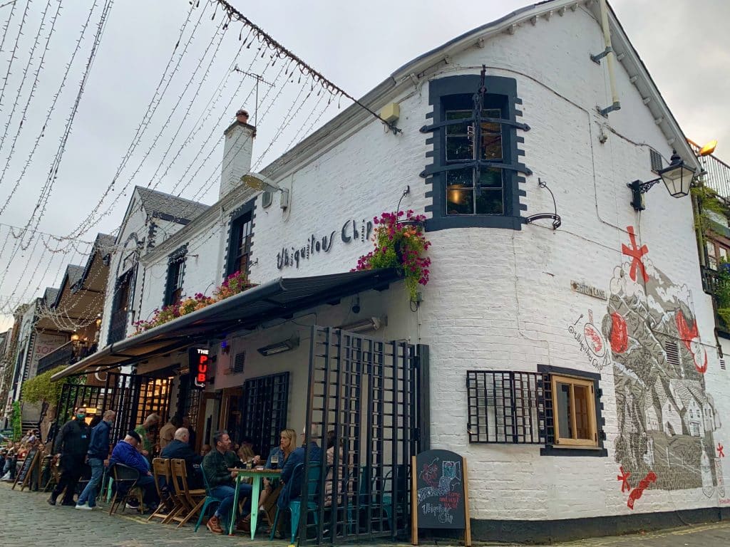 48 hours in Glasgow: the exterior of the Ubiquitous Chip with people sitting outside having a drink. The side white brick wall has some relevant street art on it.