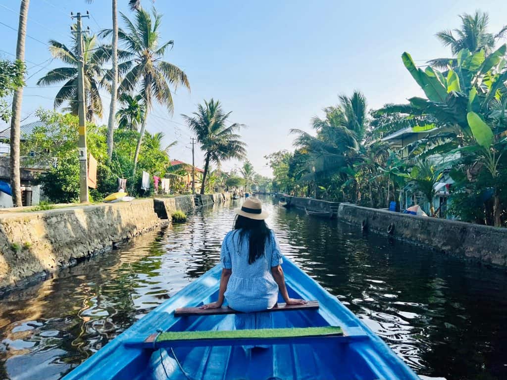 Kerala backwaters canal with Bejal sitting on fishing boat with palm trees and village life to the left and right