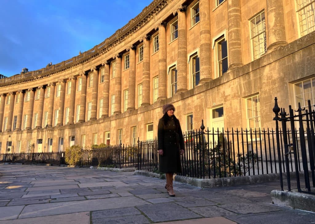 Bejal walking down The Royal Crescent wearing a faux fur hat, khaki wool coat and tan boots at golden hour in Bath 